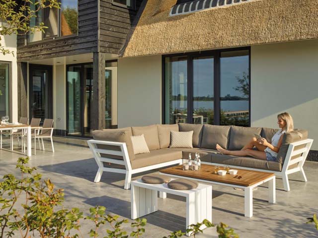 Havemøbler på terrasse med L-formet udesofa, tilhørende sofabord samt spisebord og havestole i baggrunden
